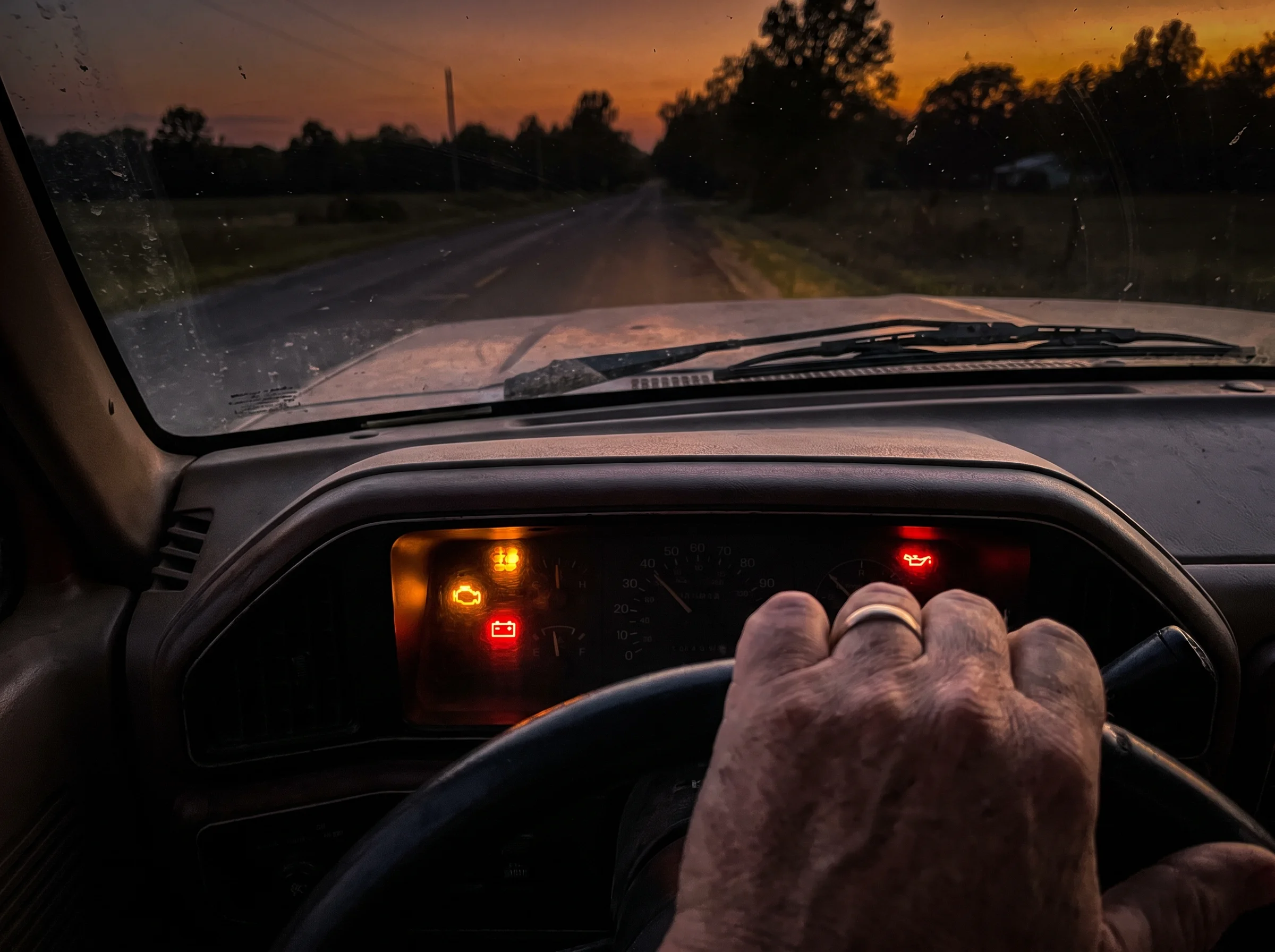 close-up of a truck dashboard with multiple warning lights lit up at once, shot at dusk through the windshield, moody amber t