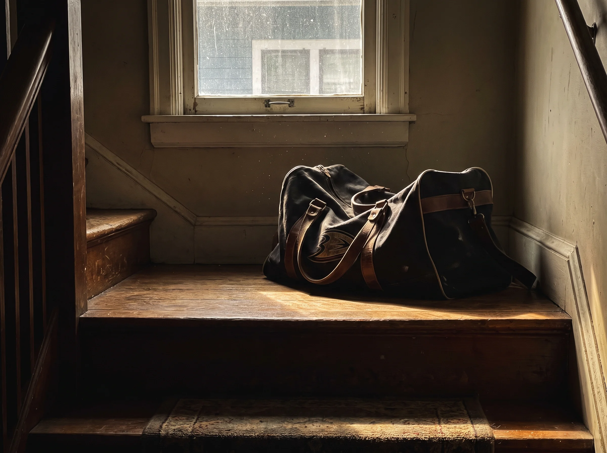 A canvas hockey bag sitting alone on a residential staircase landing, morning light through a window, no person in frame. Qui