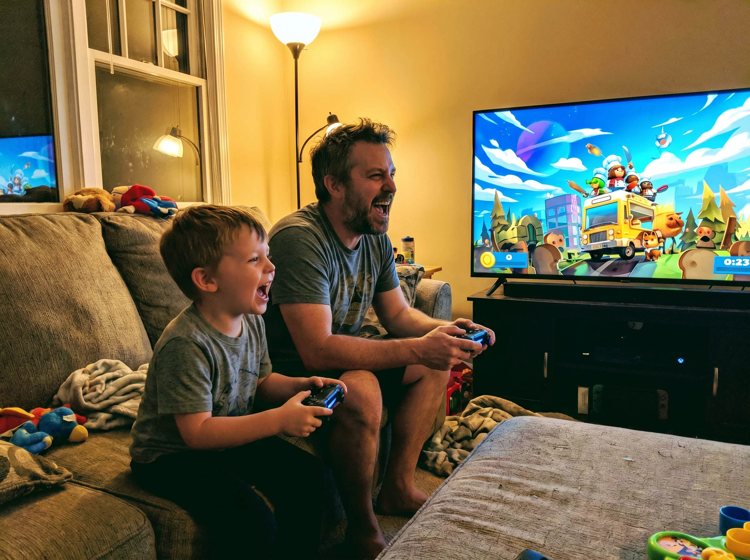 A dad and son side by side on a couch holding controllers, TV screen showing a chaotic colorful kitchen game, both leaning fo