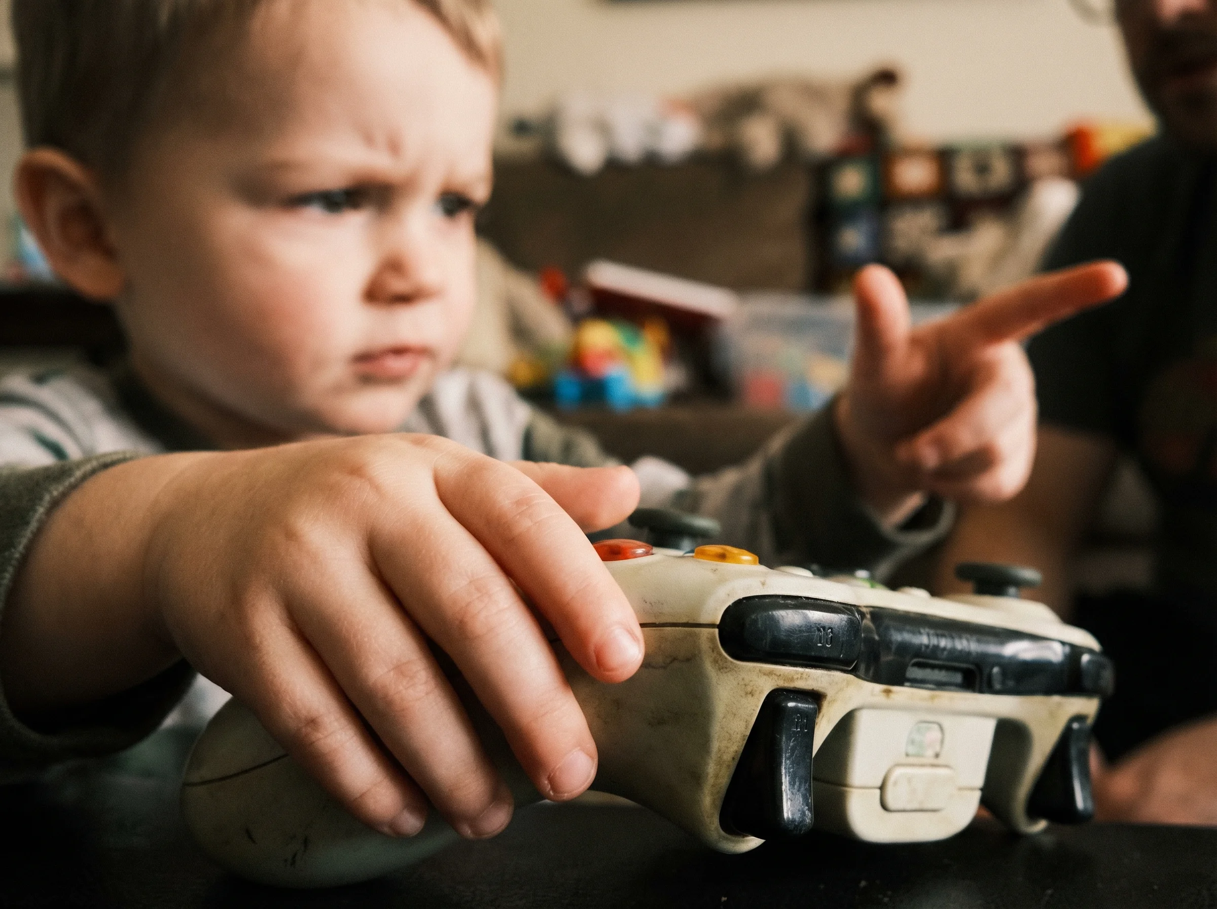 Close-up of a child's hands on a controller, focused expression visible in the background, explaining something to someone of