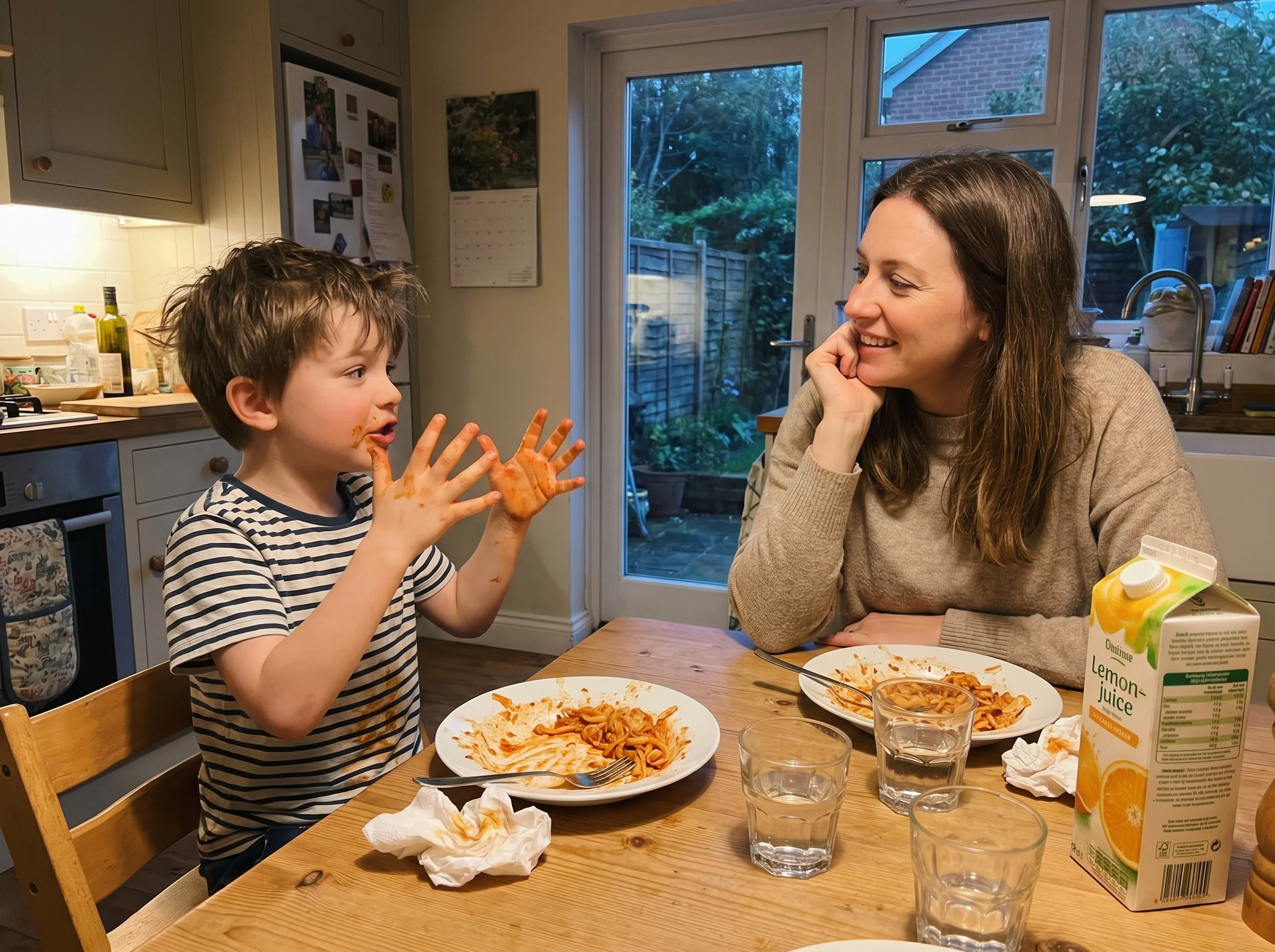 A mom and young son at the kitchen table after dinner, the boy talking animatedly with his hands, mom leaning in listening, h