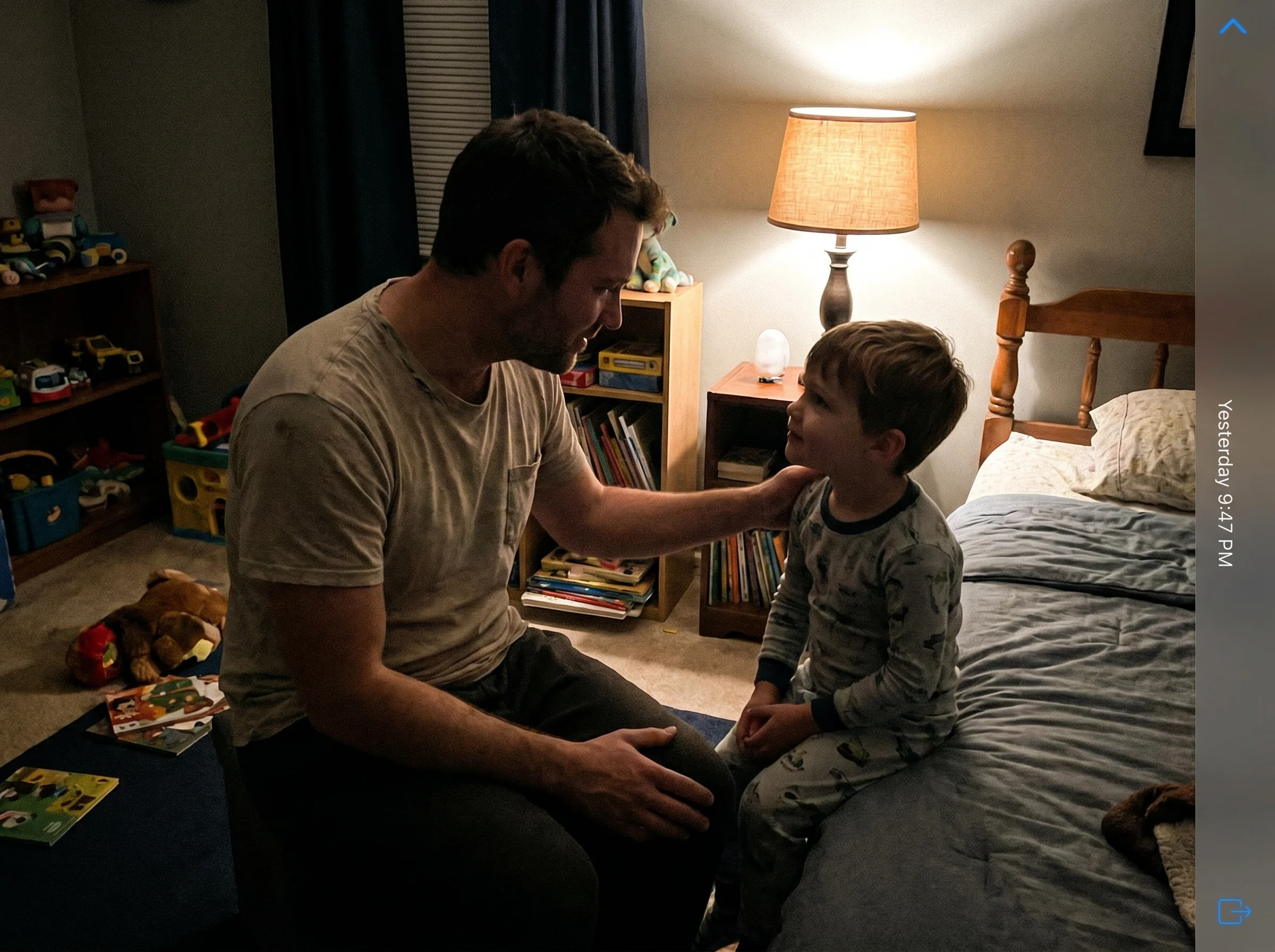 A dad sitting on the edge of a kid's bed at night, hand on his son's shoulder, both looking at each other in soft lamplight, 