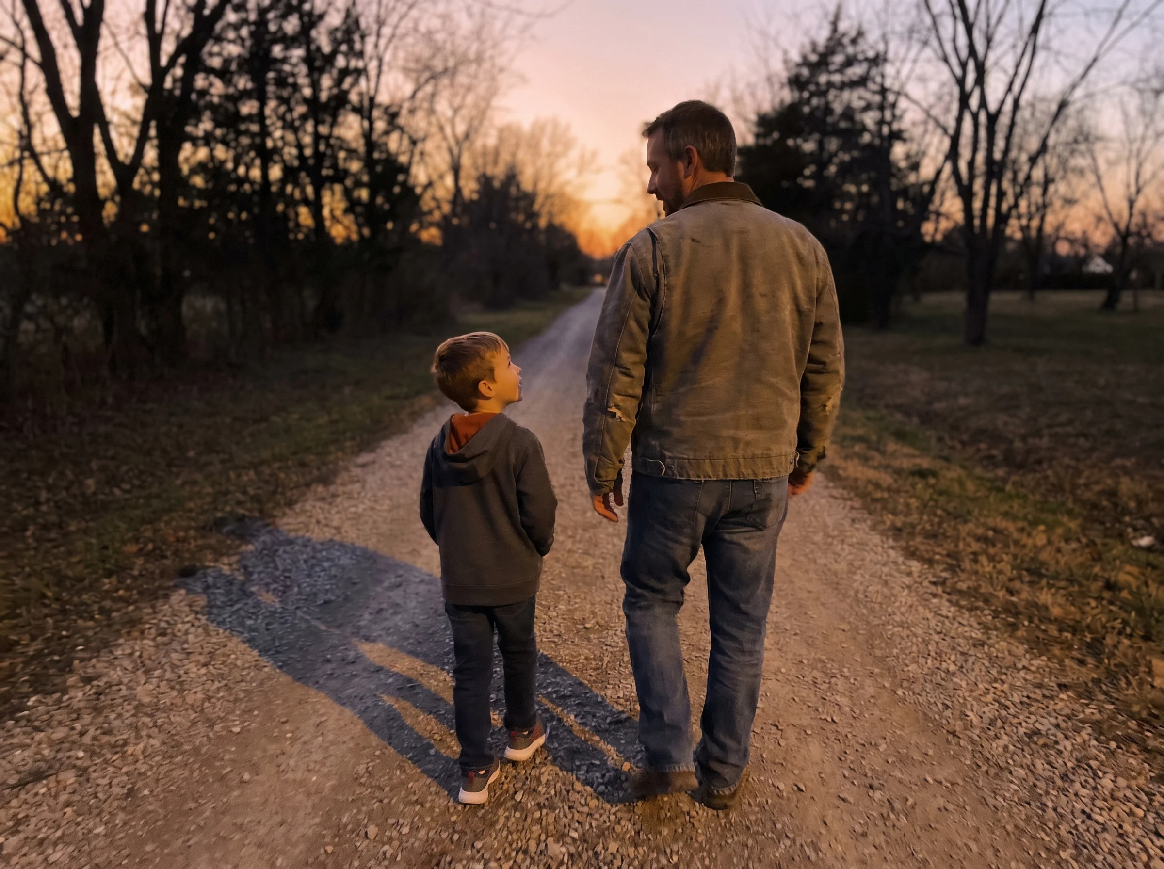 A dad and son walking outside together at dusk, backs to the camera, casual conversation, golden hour light