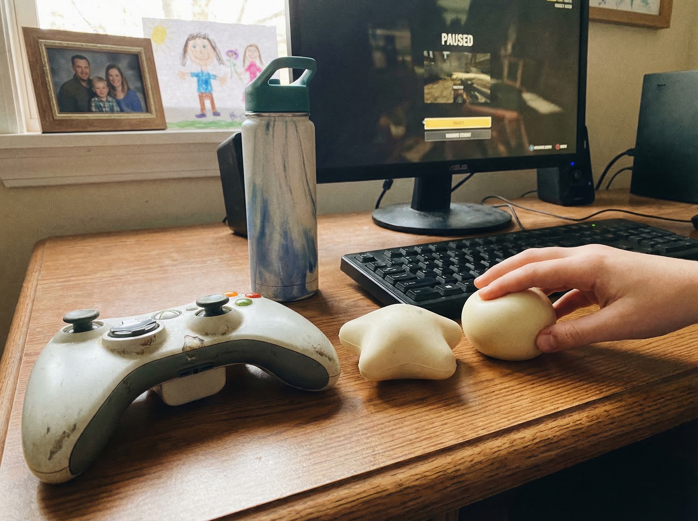 Close-up of gaming setup with stress balls and water bottle on desk next to controller, showing practical emotional regulatio