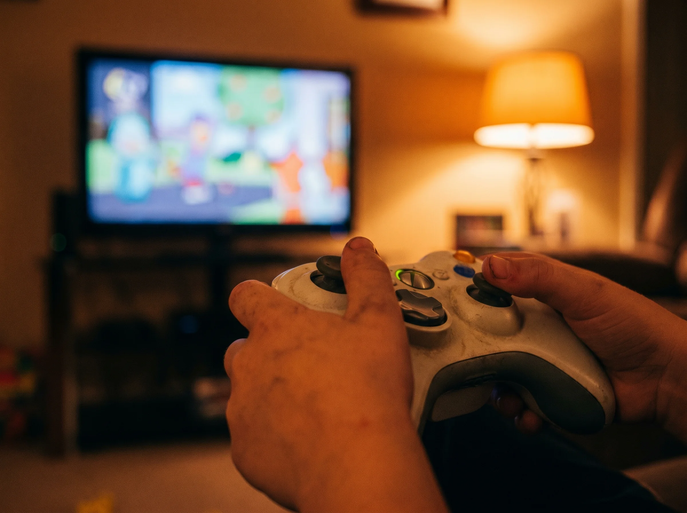 Close-up of a kid's hands holding a game controller with a slightly blurred TV screen in the background, warm tones, candid s