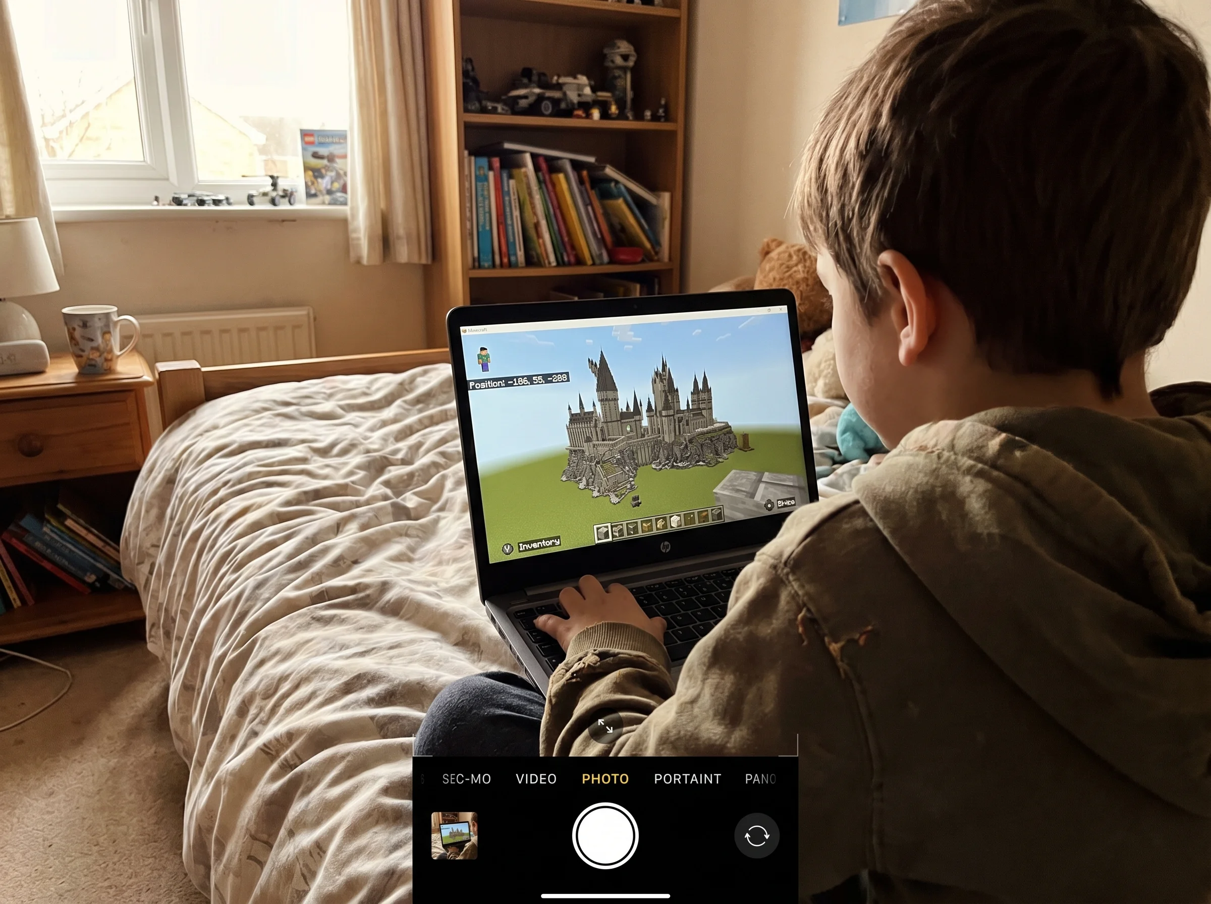 A kid building an elaborate structure in Minecraft on a laptop screen, shoulder-view from behind the kid, cozy bedroom settin