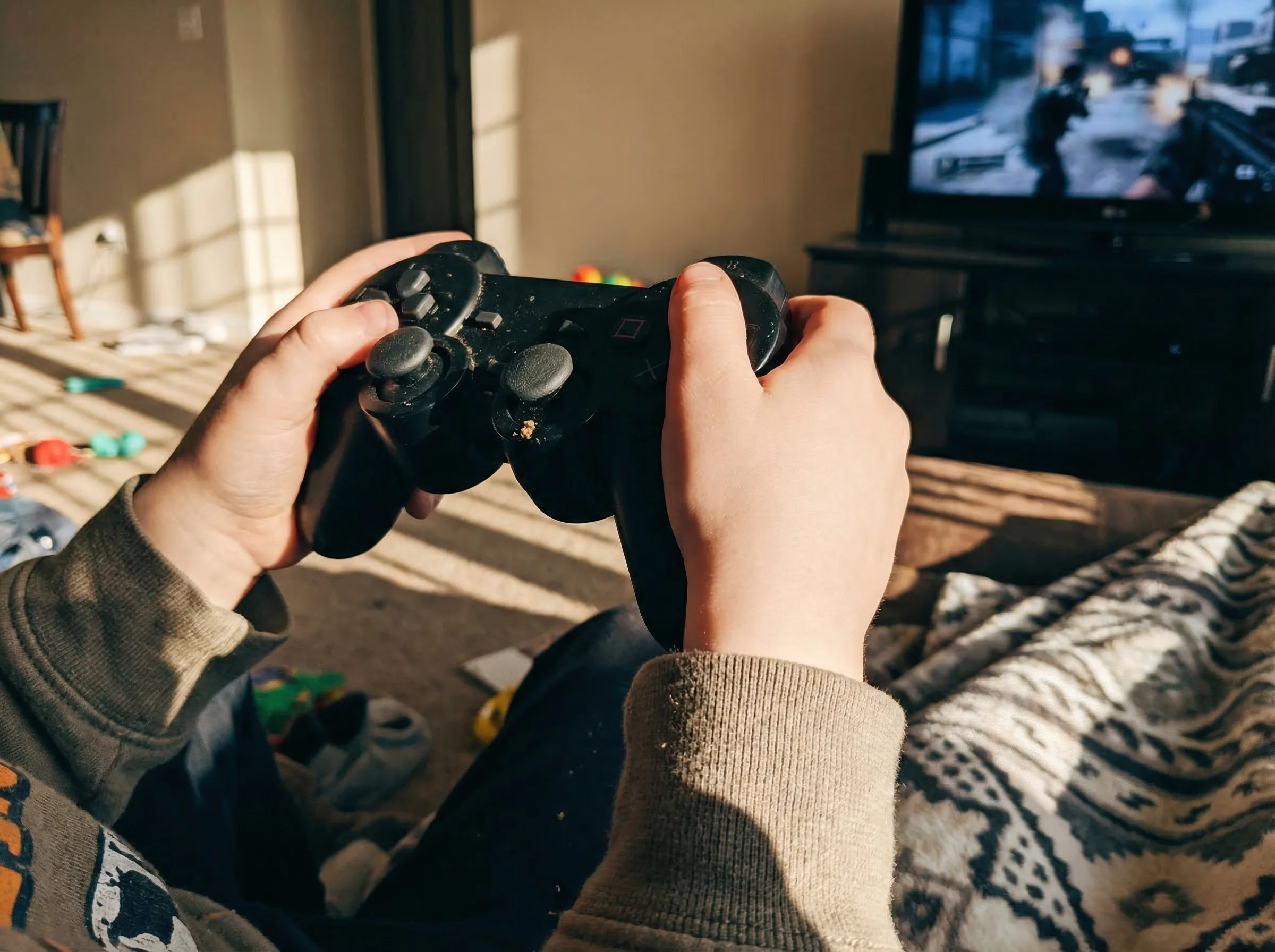 Close-up of a child's hands gripping a game controller, tension visible in their posture, focused intently on the screen with