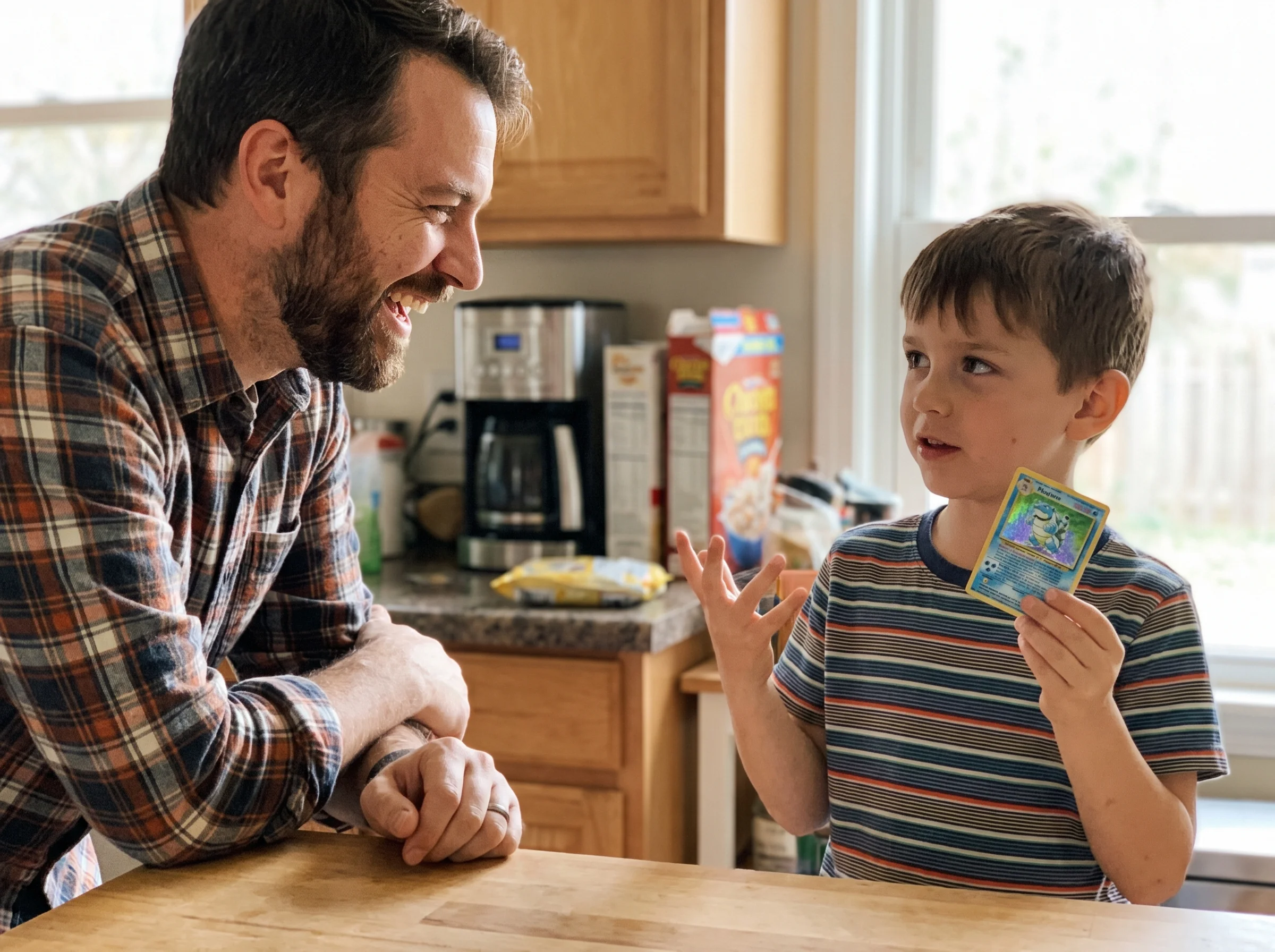 Dad laughing while his son holds up a Pokémon card, clearly explaining something with confidence, kitchen counter in the back