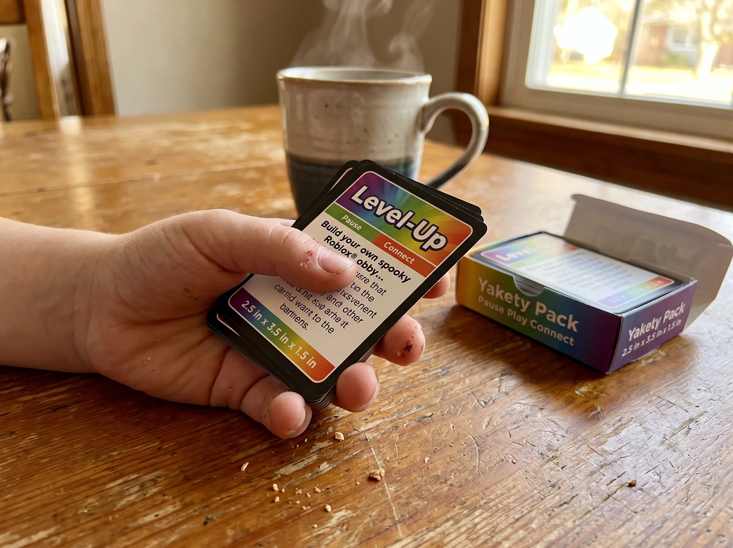 A close-up of a kid's hand holding a stack of Pokémon trading cards on a kitchen table, parent's coffee mug in the background