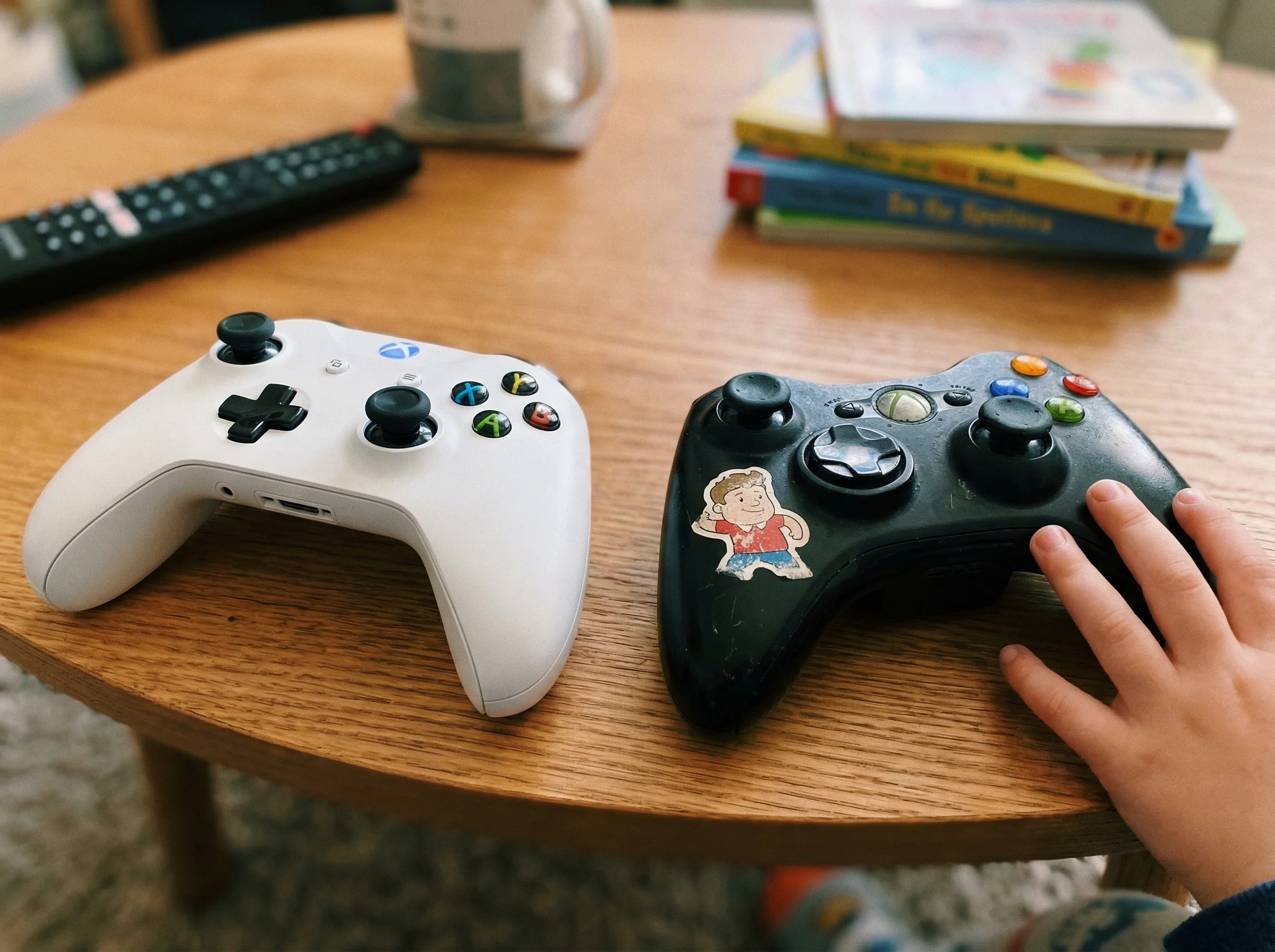 Close-up of two different game controllers side by side on a coffee table, one newer and one showing wear, highlighting the v