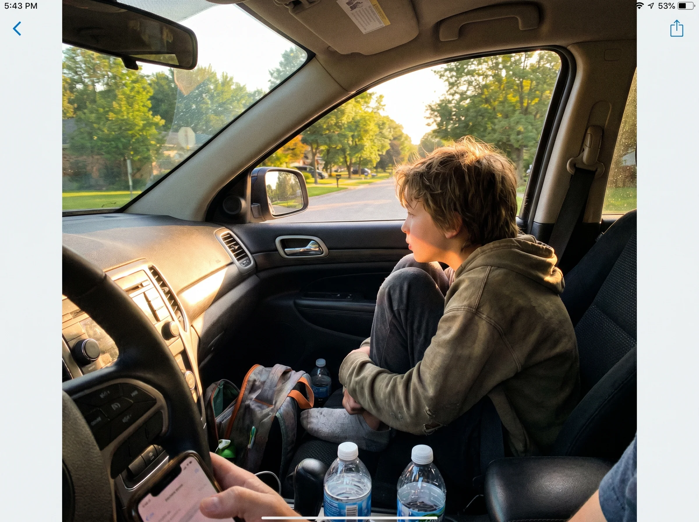 View from the driver's seat of a car, a kid in the passenger seat looking out the window, golden hour light, casual and relax