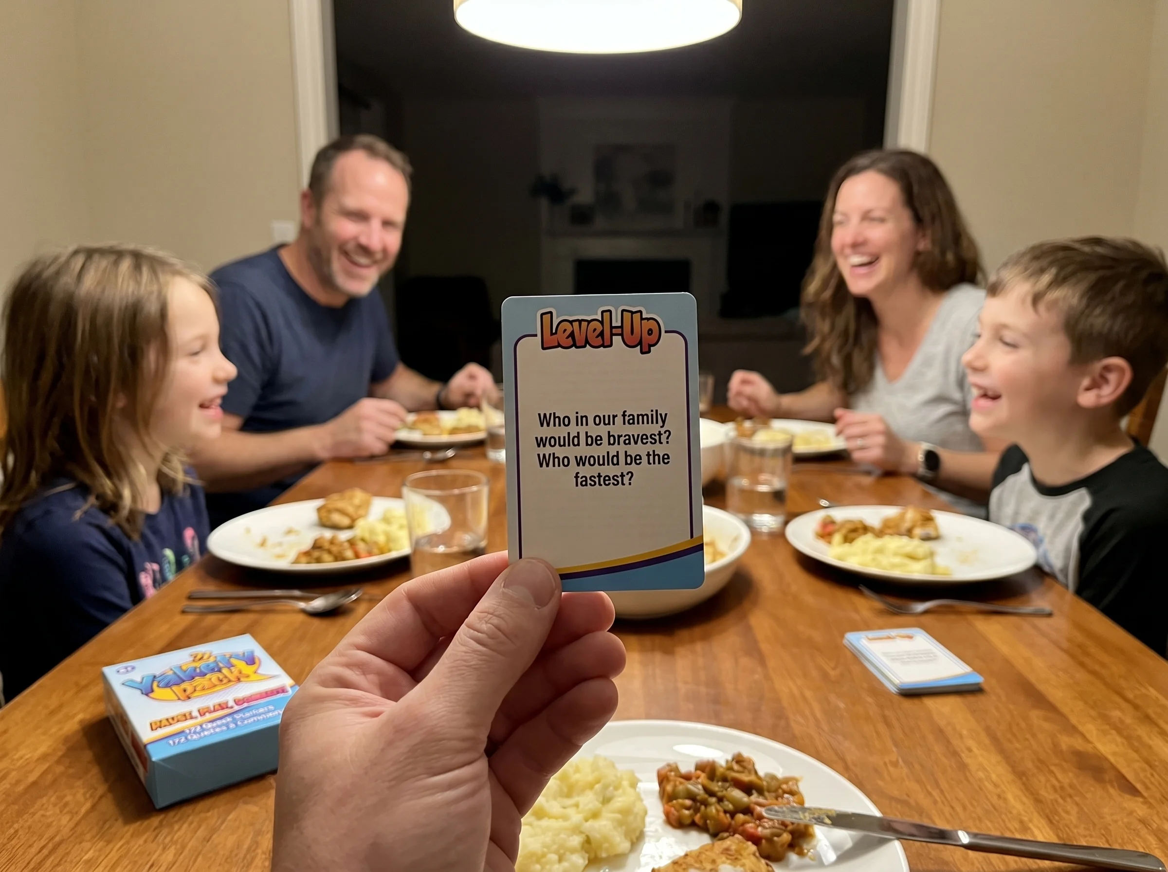 A Yakety Pack conversation card being held up at a dinner table, family members slightly blurred in the background, warm over