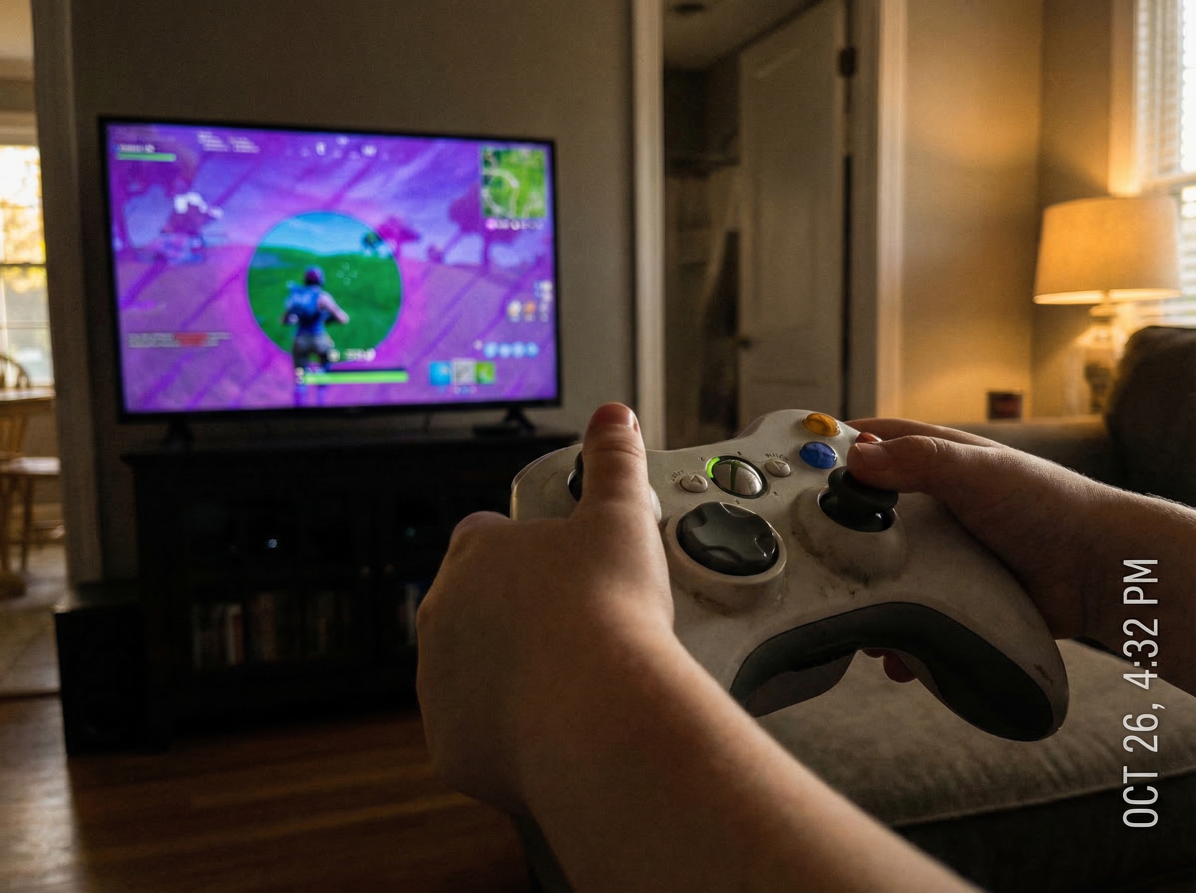 Close-up of a Fortnite game on screen showing an active match with the storm closing in, a child's hands visible on the contr