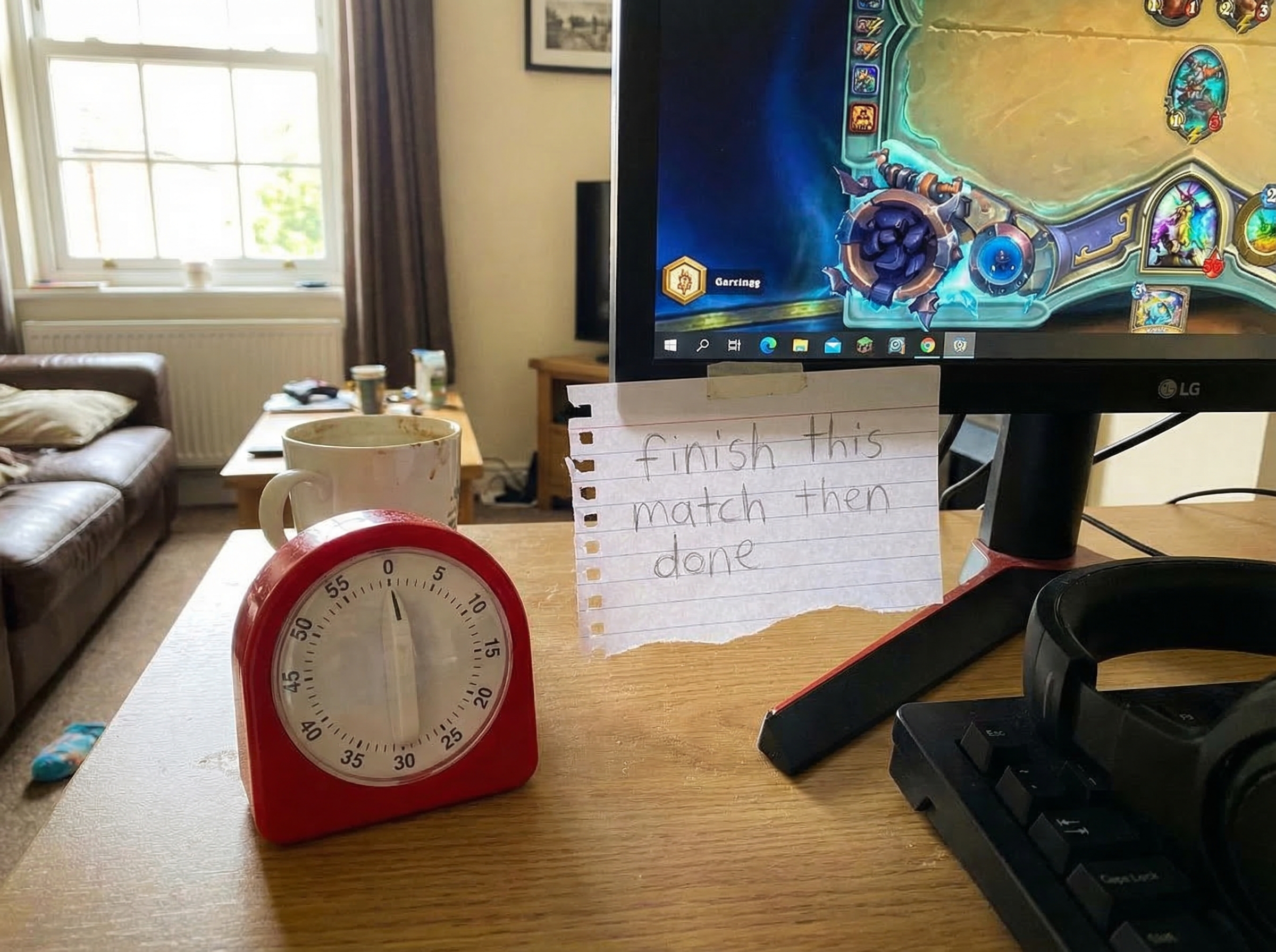 A kitchen timer sitting next to a gaming setup, with a handwritten note that says "finish this match then done" visible in a