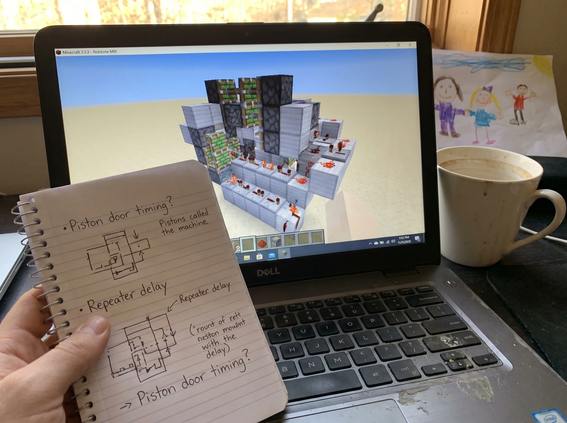 A close-up of a Minecraft build on a computer screen, an elaborate redstone contraption with notes scribbled on a notepad nex