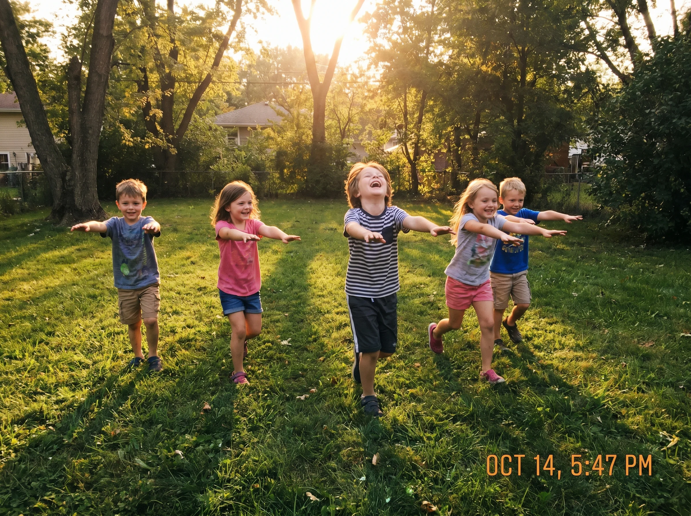 A group of elementary-age kids running across a grass yard with arms outstretched zombie-style, one laughing hard, golden hou