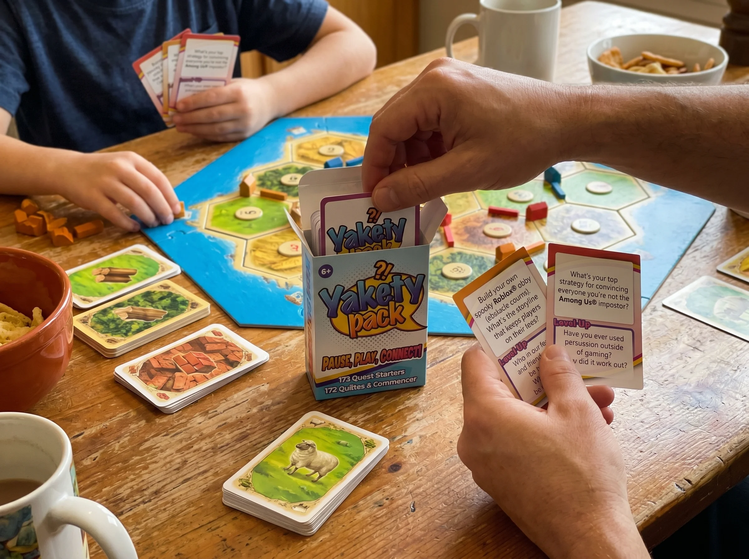 close-up of hands moving wooden pieces on a Catan-style board, scattered resource cards visible, warm kitchen table lighting