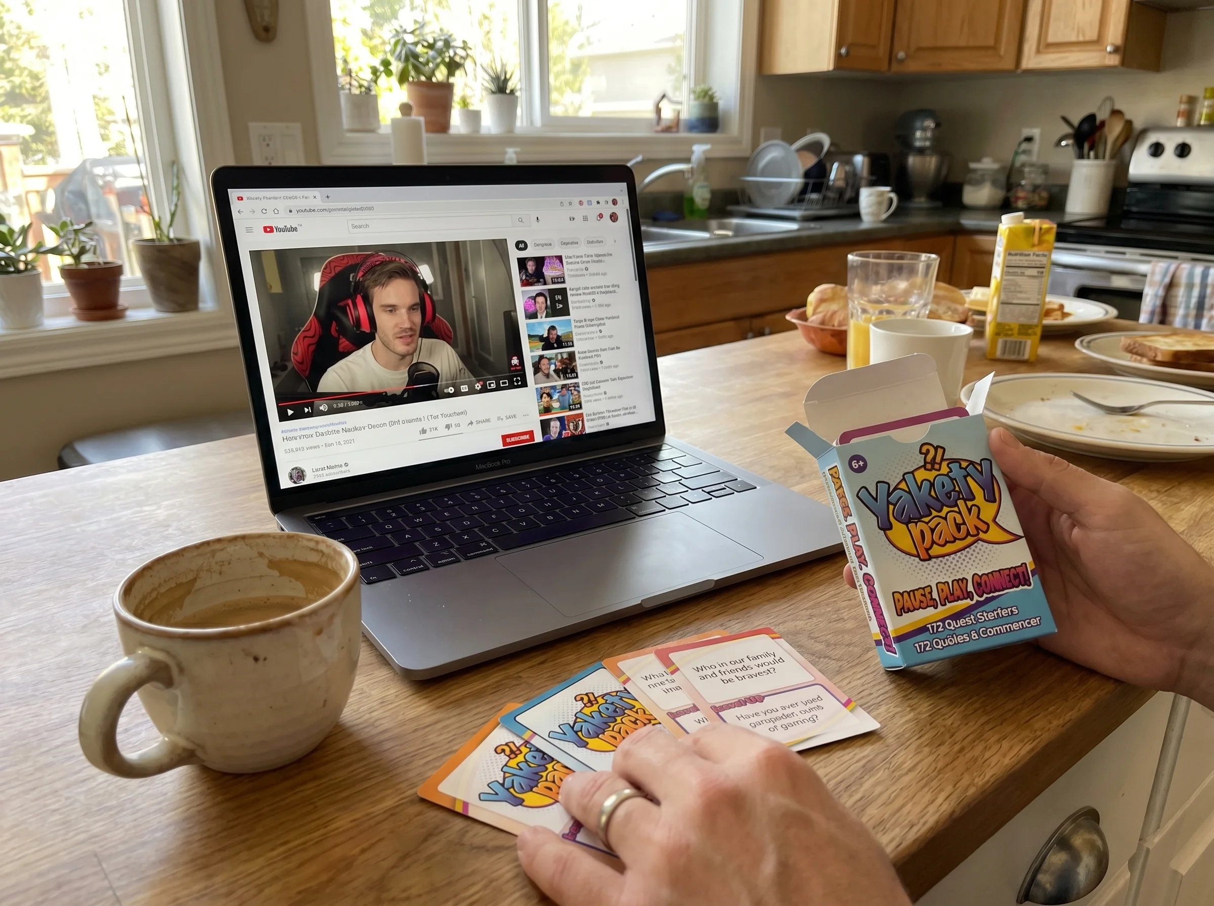 A laptop on a kitchen counter with a paused YouTube streamer video on screen, coffee mug nearby, morning light, parent perspe