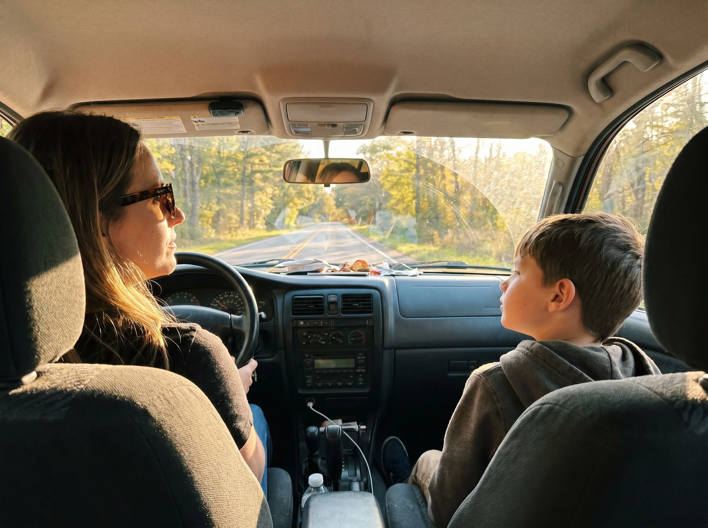 A parent and a kid in a car, parent driving, kid in the passenger seat looking out the window, soft afternoon light, real can