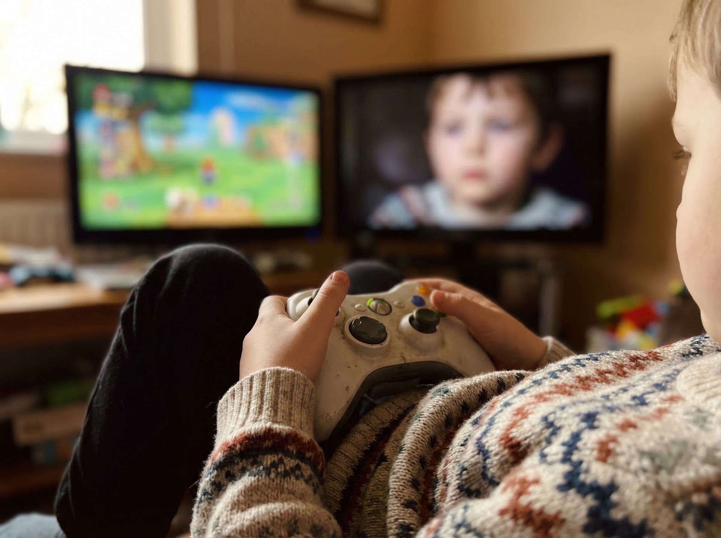 Close-up of child's hands on controller, shoulders visibly relaxed, focused but calm expression reflected in TV screen