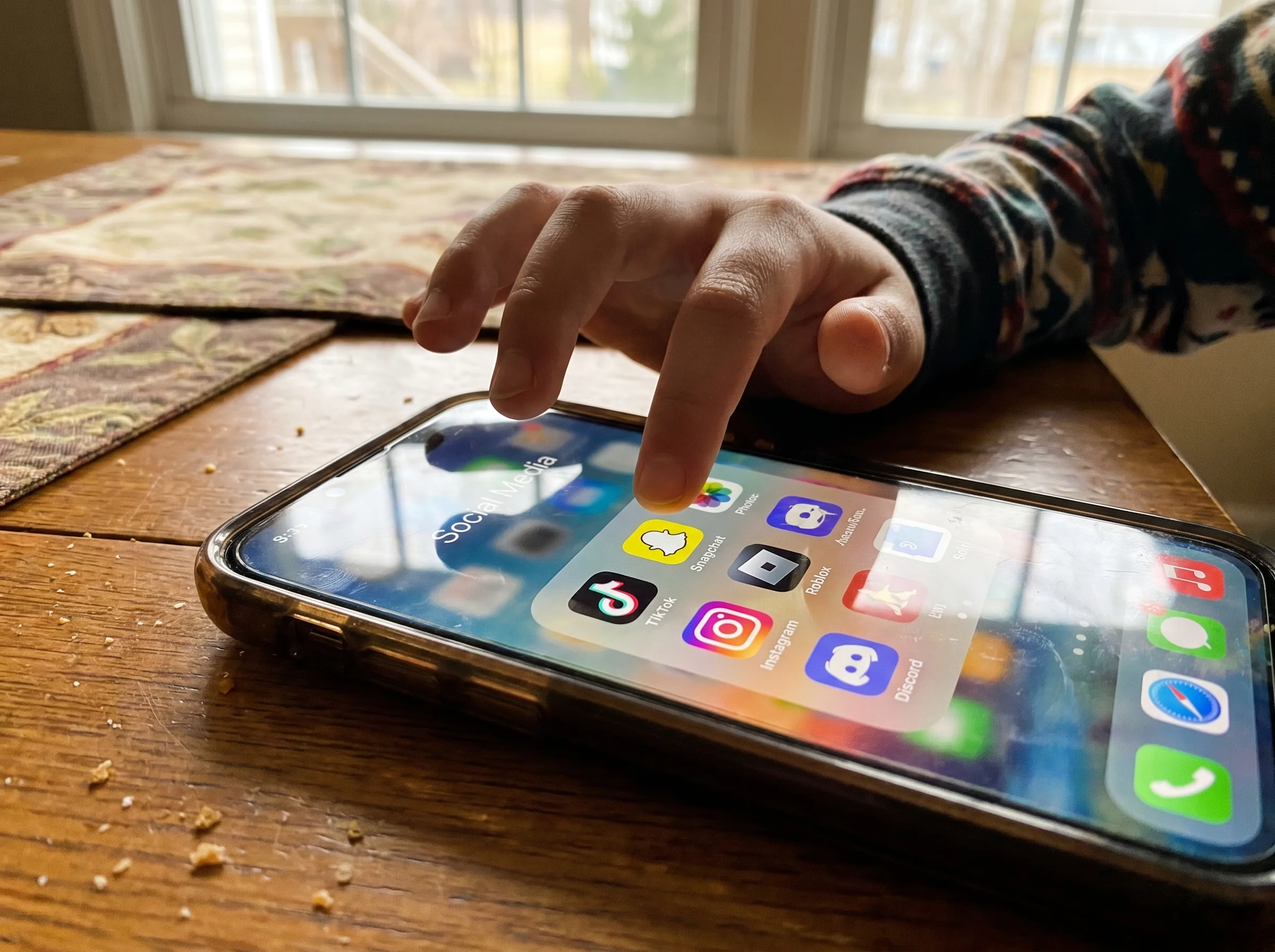 Close-up of a middle schooler's phone home screen showing colorful social and gaming app icons, finger hovering over Snapchat