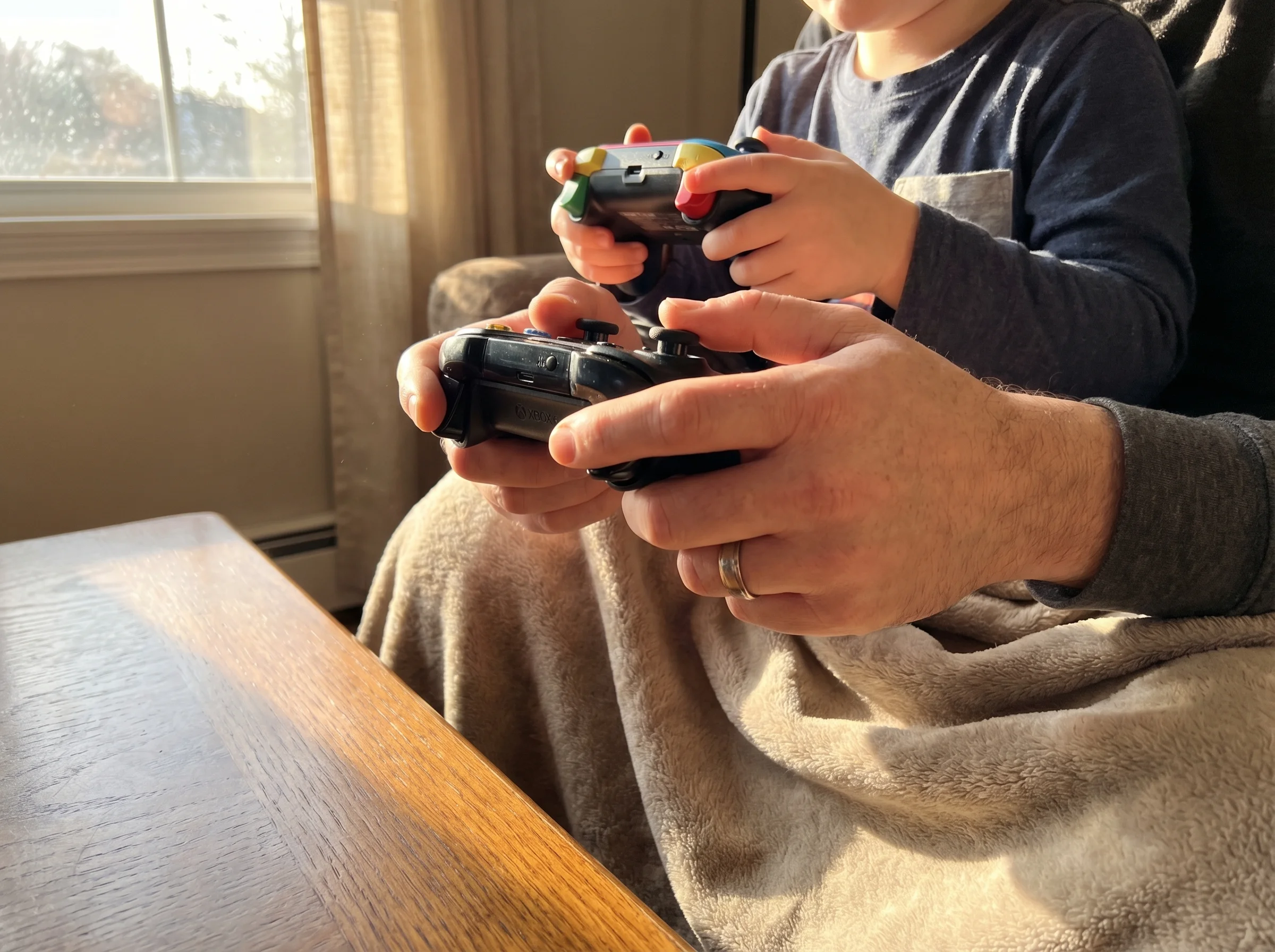 Close-up of two sets of hands holding controllers, one adult and one child, natural afternoon light streaming through window