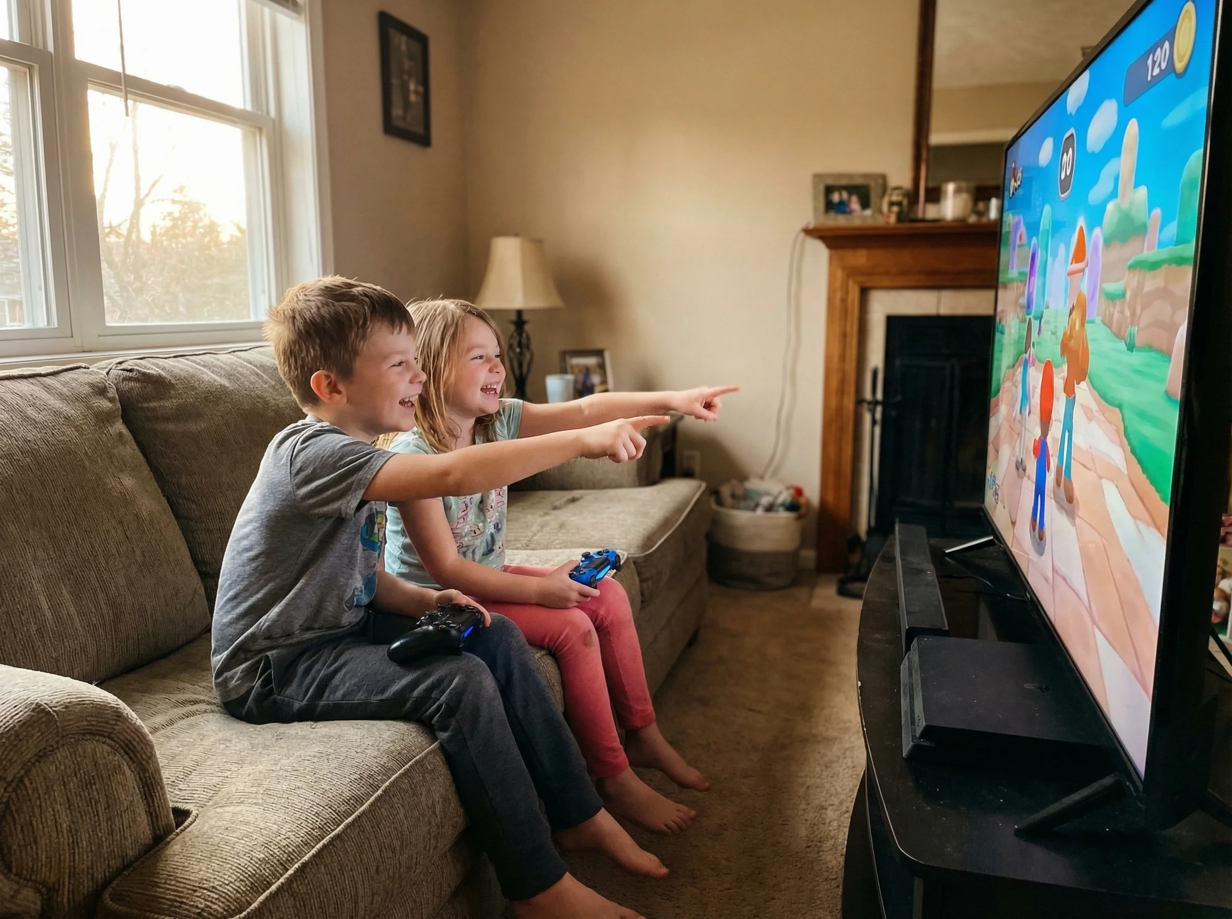 Two kids on a couch, game controllers in hand, leaning toward each other excitedly while looking at a TV screen, one pointing