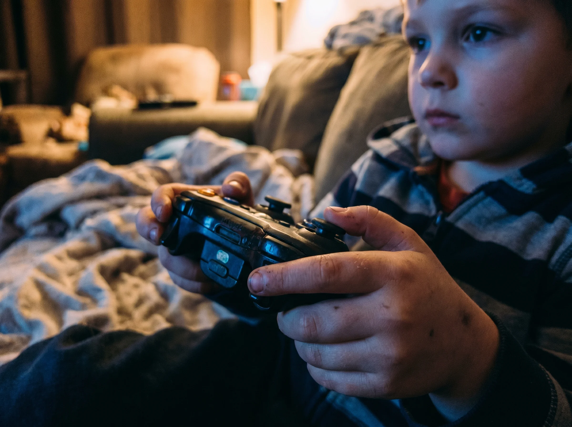 Close-up of a kid's hands holding a game controller, focused expression visible in background, lit by the glow of a TV screen