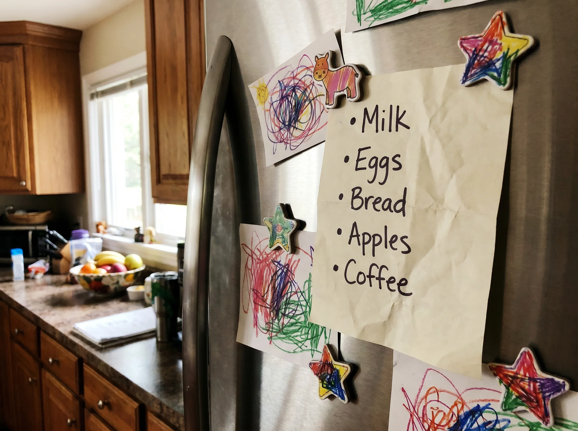 A handwritten list on the fridge with simple bullet points, slightly crumpled, kid's drawing magnets around it, casual home k