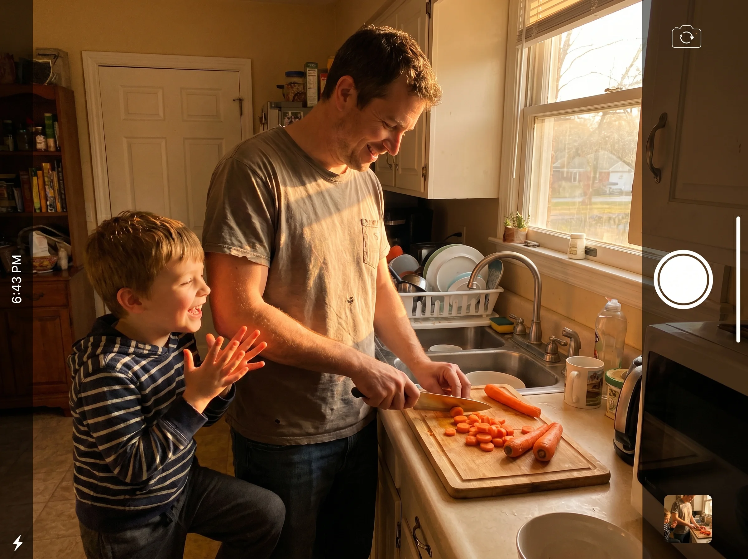 A dad chopping vegetables at a kitchen counter while his son leans against the counter beside him talking animatedly, warm ev