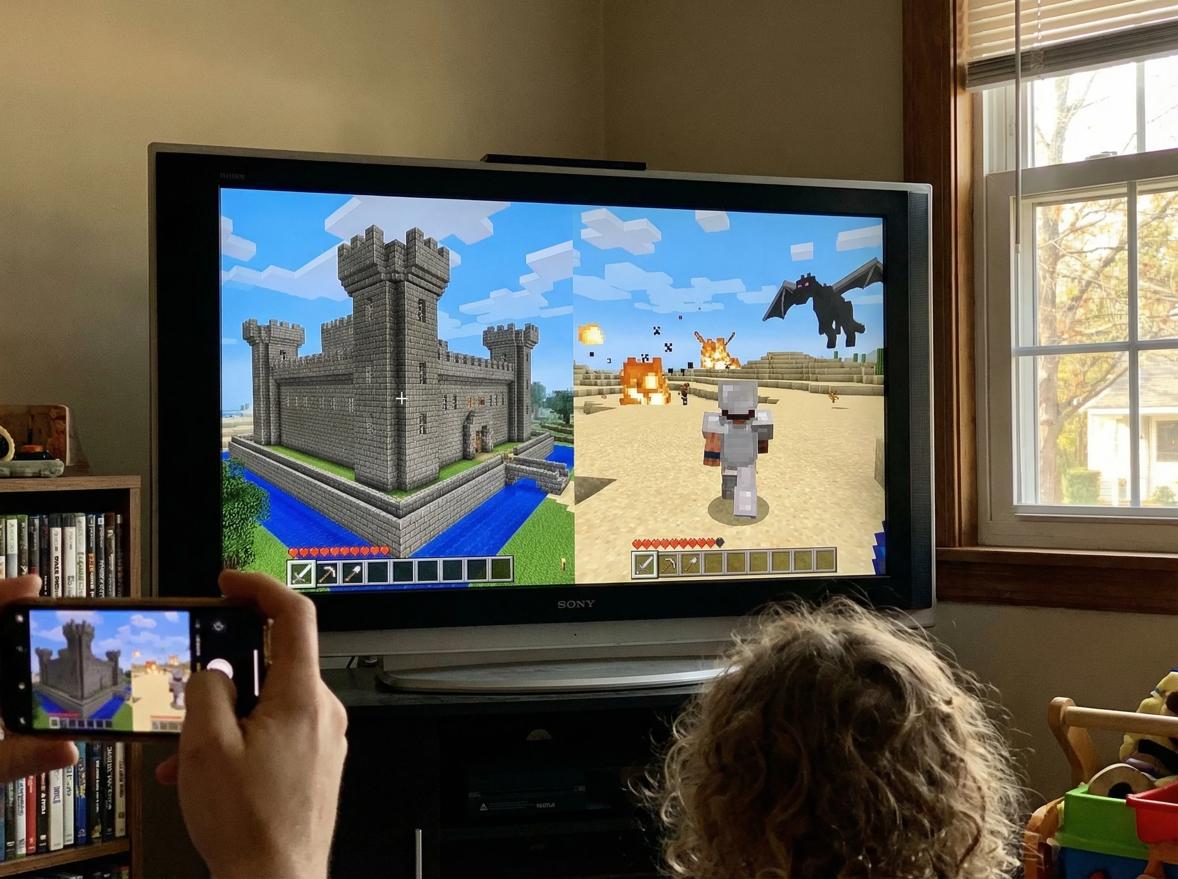 A split-screen view on a TV showing two different Minecraft worlds - one with an elaborate castle, the other with adventure e