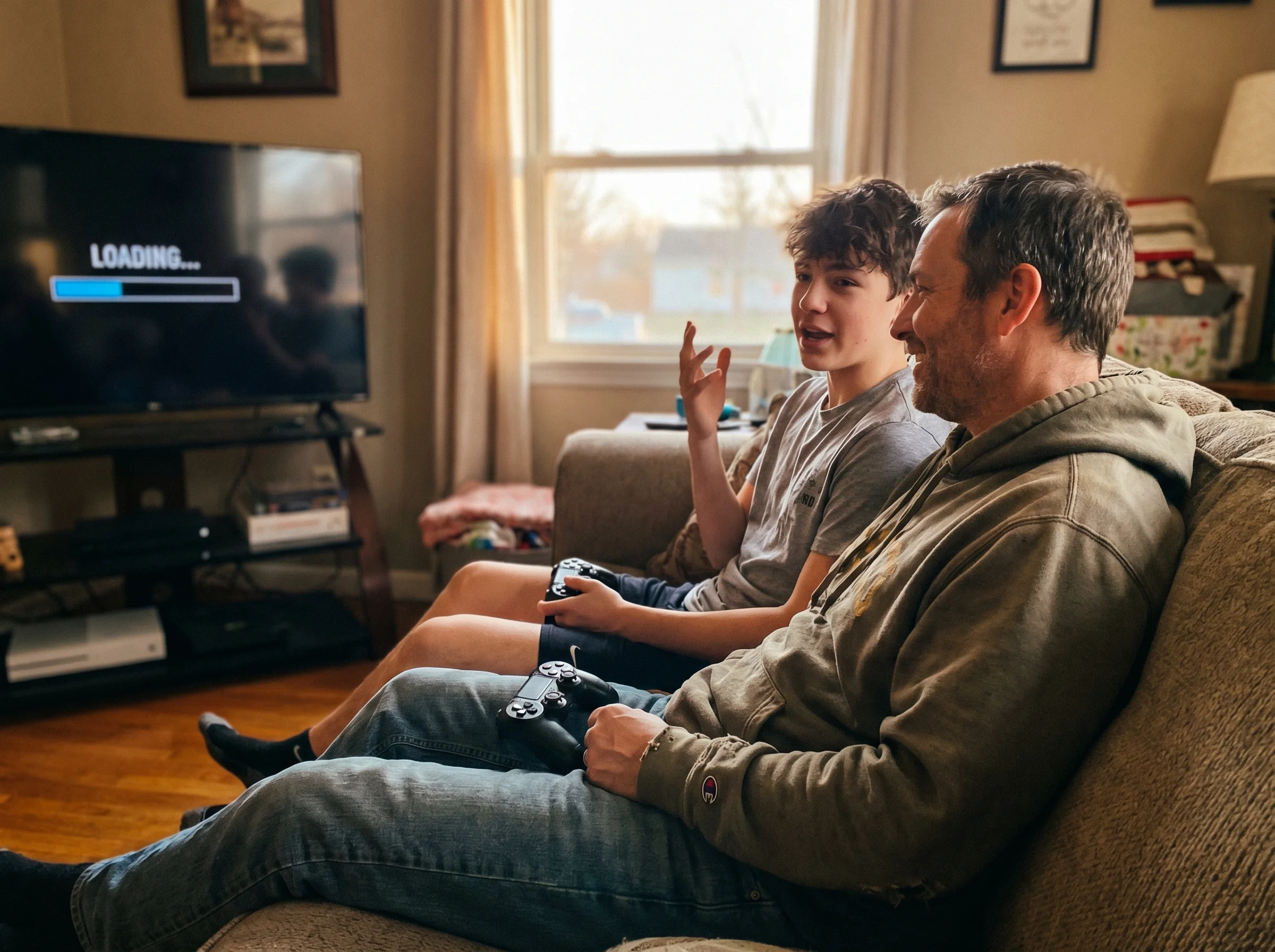 Parent and teen sitting close together on couch during a game loading screen, teen gesturing while talking, parent listening