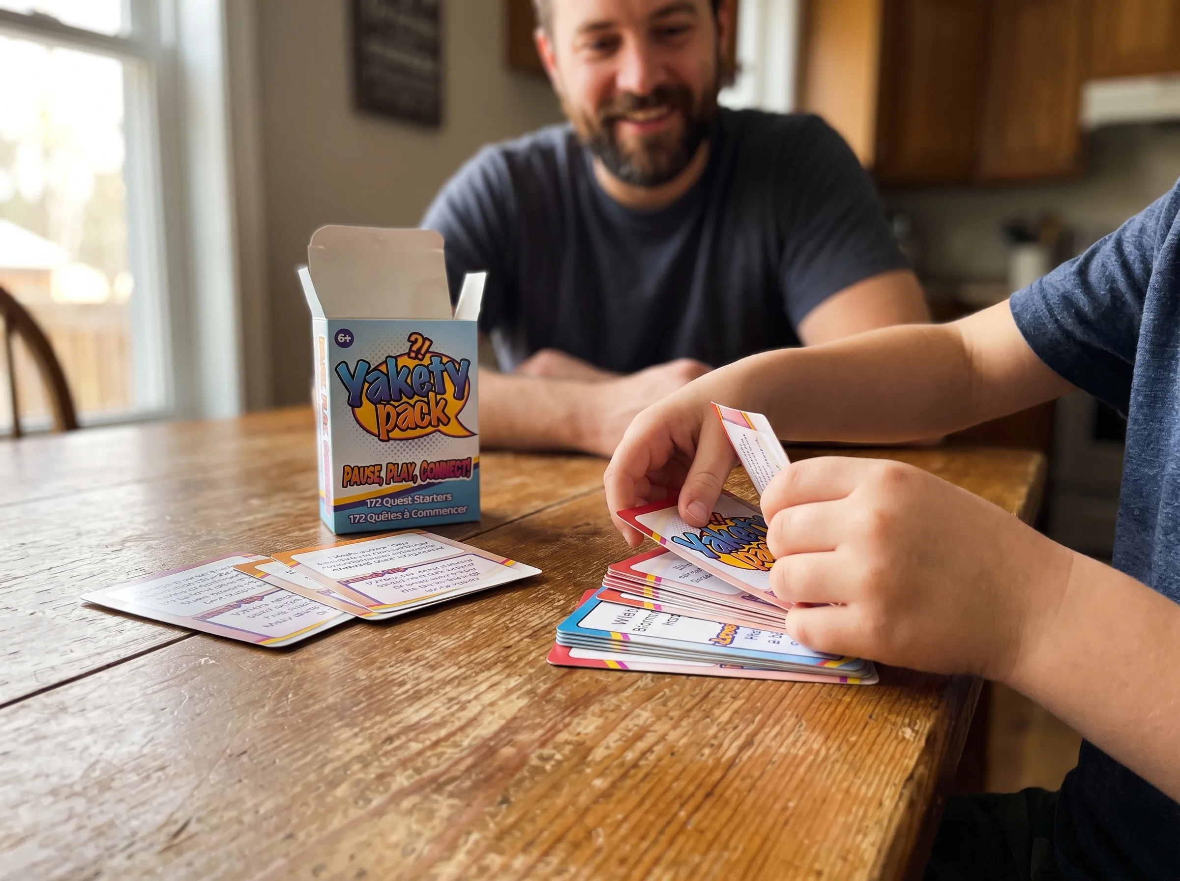 Close up of a kid's hands sorting through a stack of Pokémon cards on a wooden kitchen table, slightly out of focus dad in ba