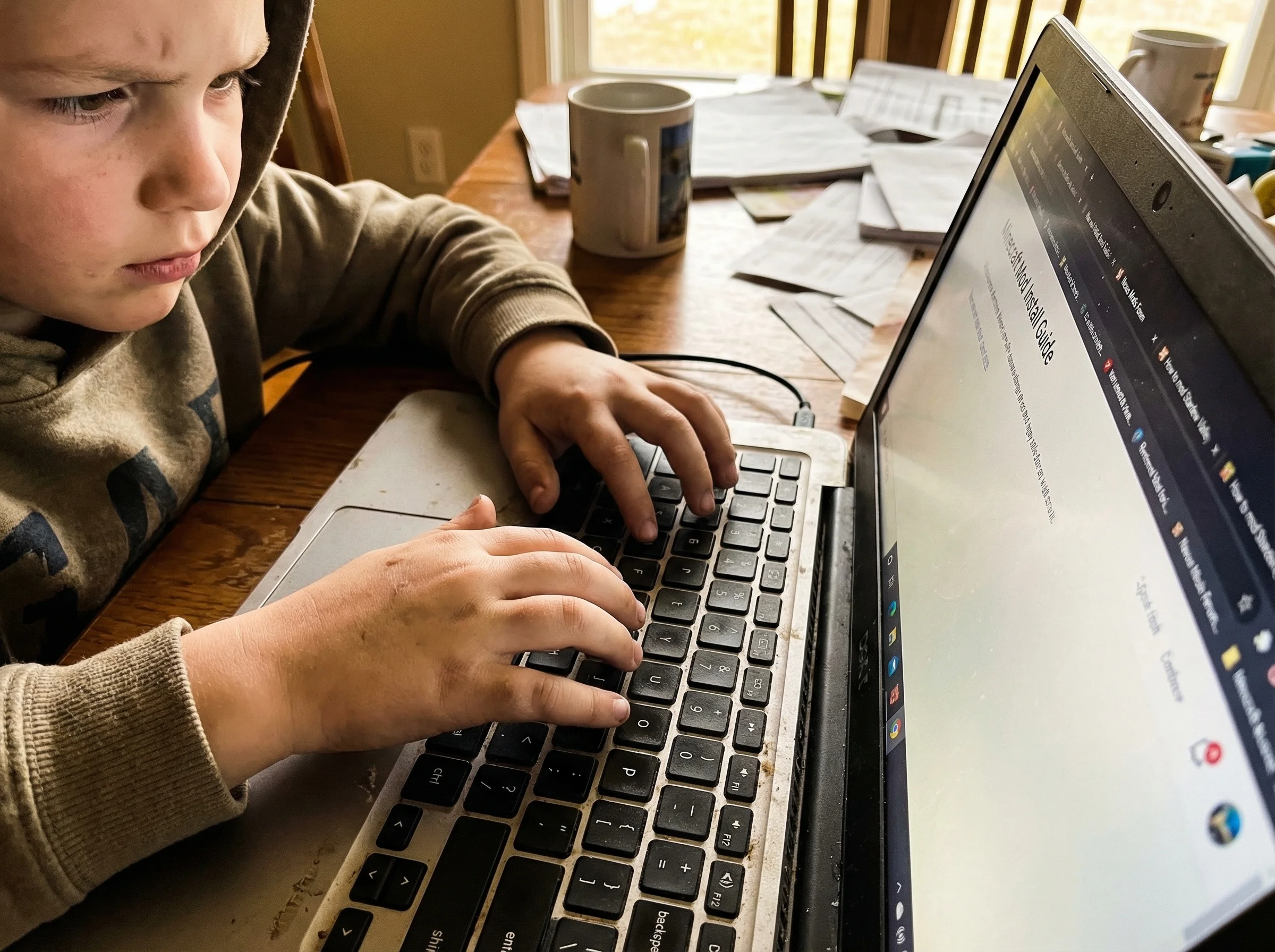 Close-up of child's hands on keyboard, multiple browser tabs open showing mod installation tutorials and forums, determined c