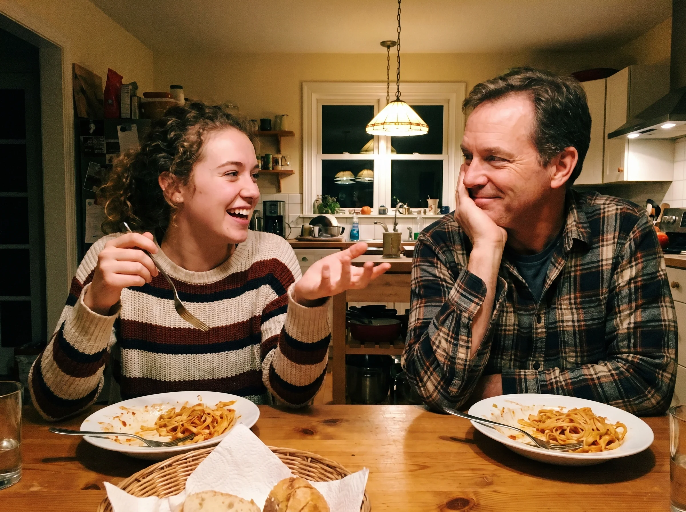 A daughter mid-sentence at the dinner table holding a fork, dad listening with chin in hand, plates of pasta in the foregroun