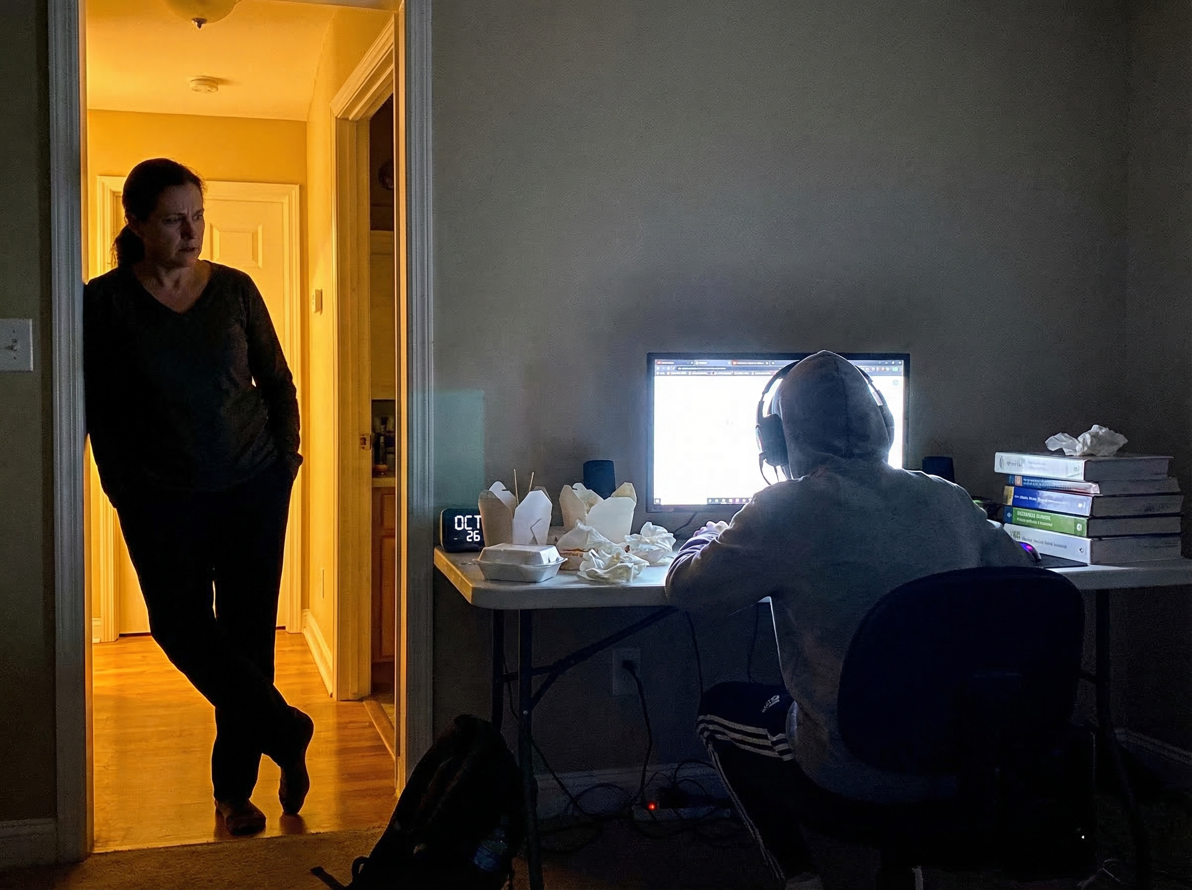 A worried parent watching their child from the doorway, the kid completely absorbed in gaming with empty food plates and unto